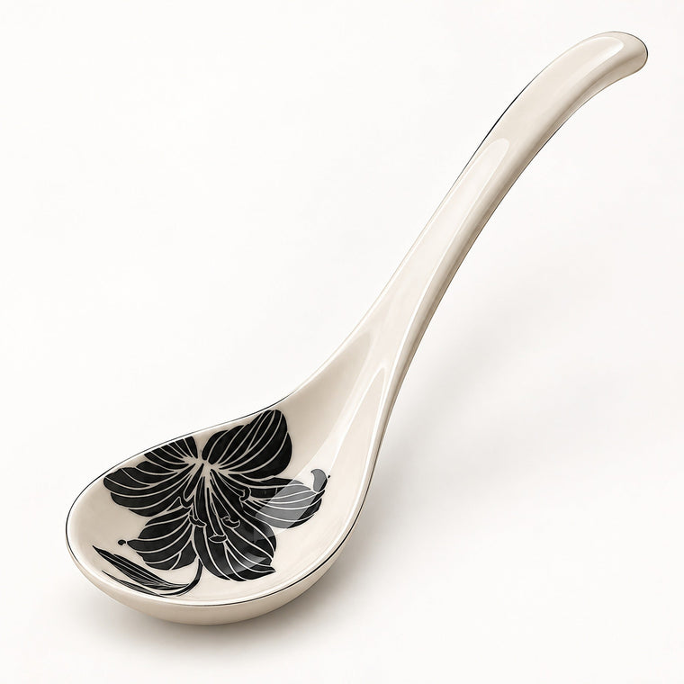 An off-white ceramic serving spoon featuring a black floral pattern on the bowl, set against a clean white background