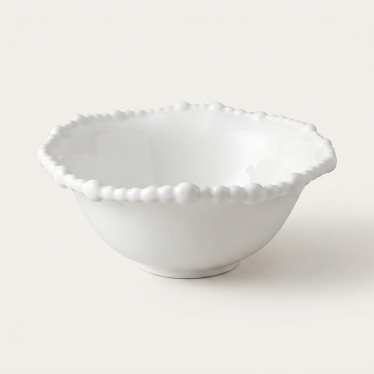 A white ceramic bowl with a scalloped, beaded rim, photographed against a clean, solid, warm off-white background