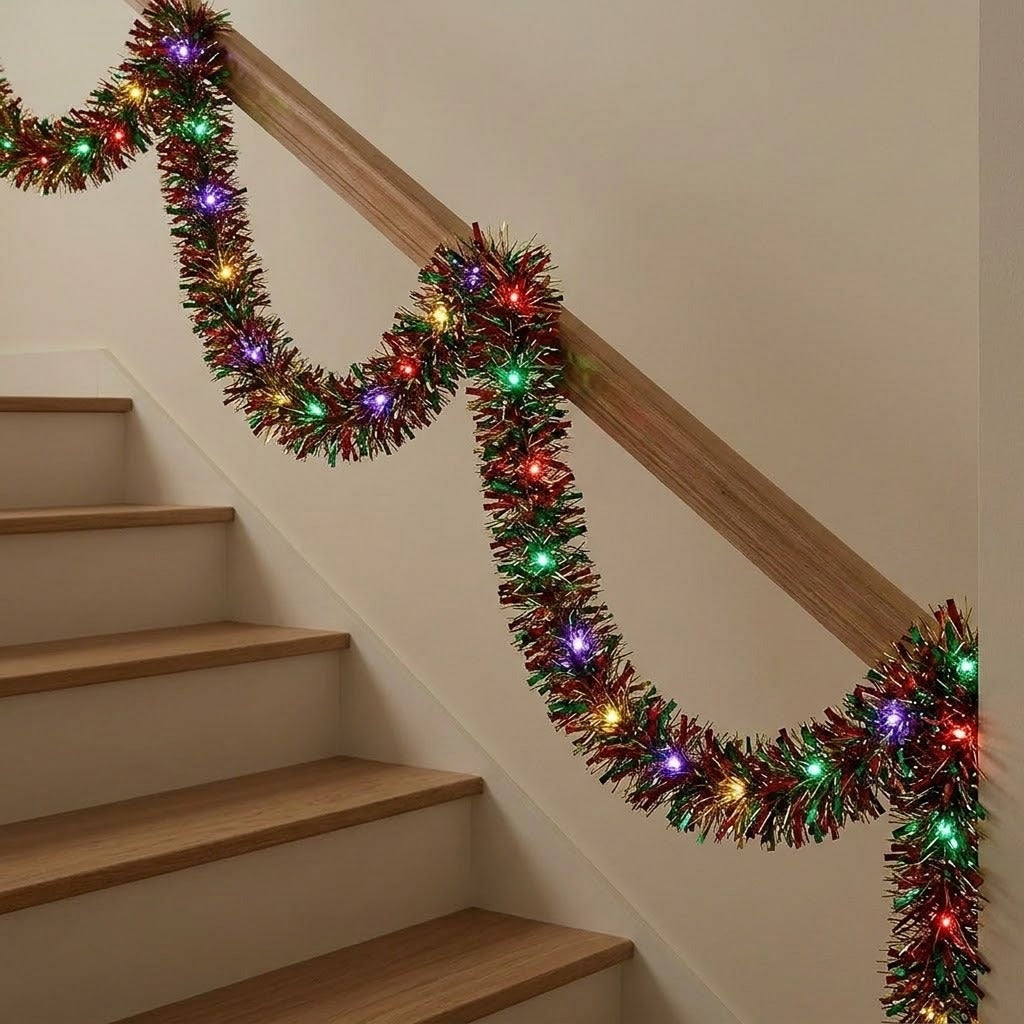A festive Christmas tinsel garland with multicolored lights draped over a wooden staircase railing in an indoor setting