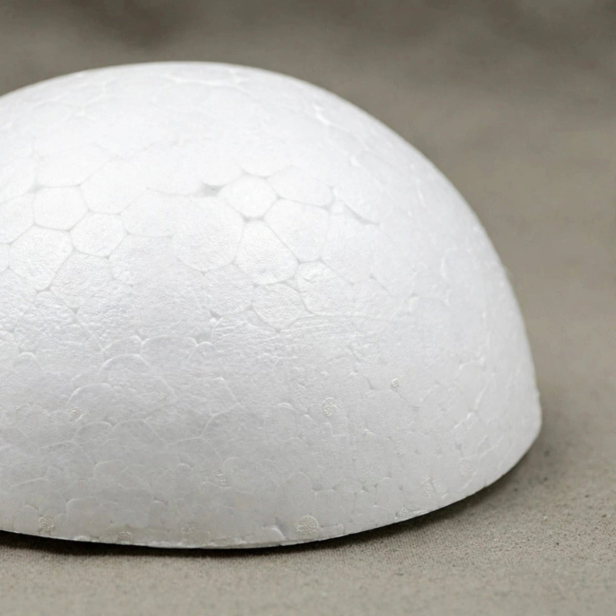 A close-up shows the bead texture and flat bottom edge of a white polystyrene foam half ball on a grey surface