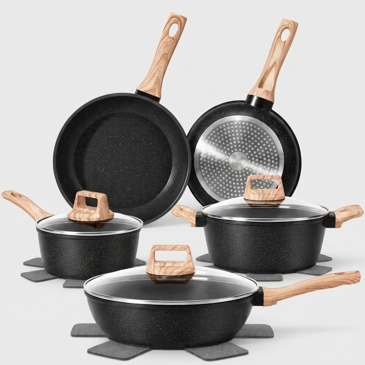 A 5-piece non-stick cookware set in black with light wood handles and lids, displayed on gray trivets against a light