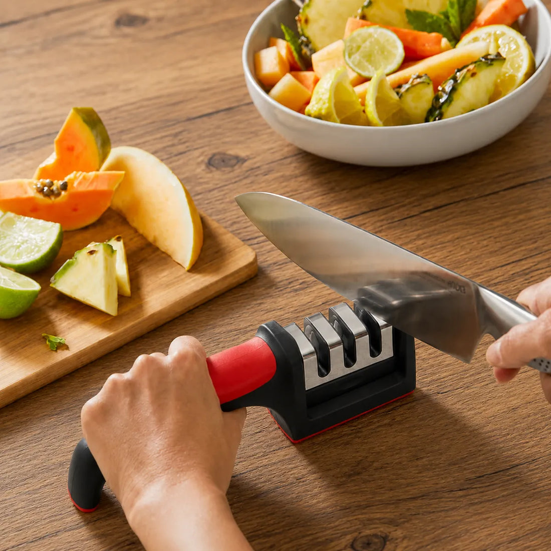 Manual pull-through knife sharpener on a kitchen table beside a bowl of fruit