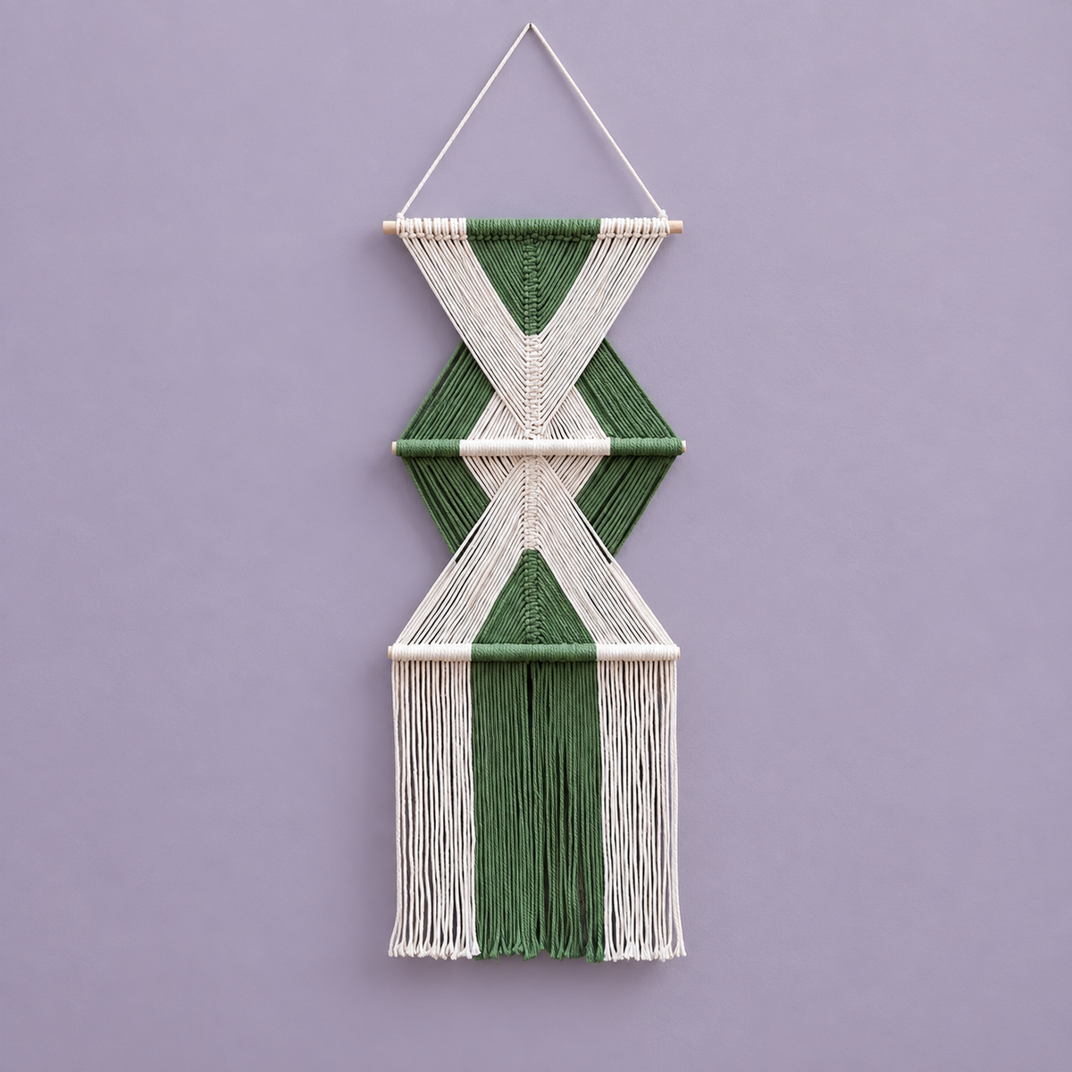 Forest green and cream macrame wall hanging on a wooden dowel against a lilac wall