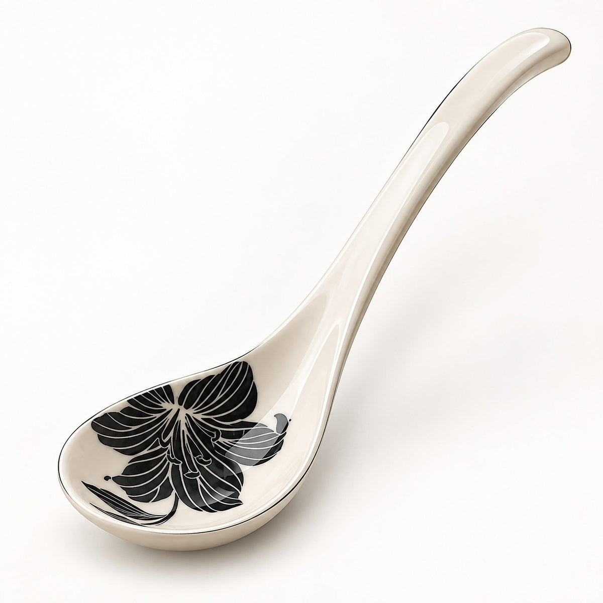 An off-white ceramic serving spoon featuring a black floral pattern on the bowl, set against a clean white background