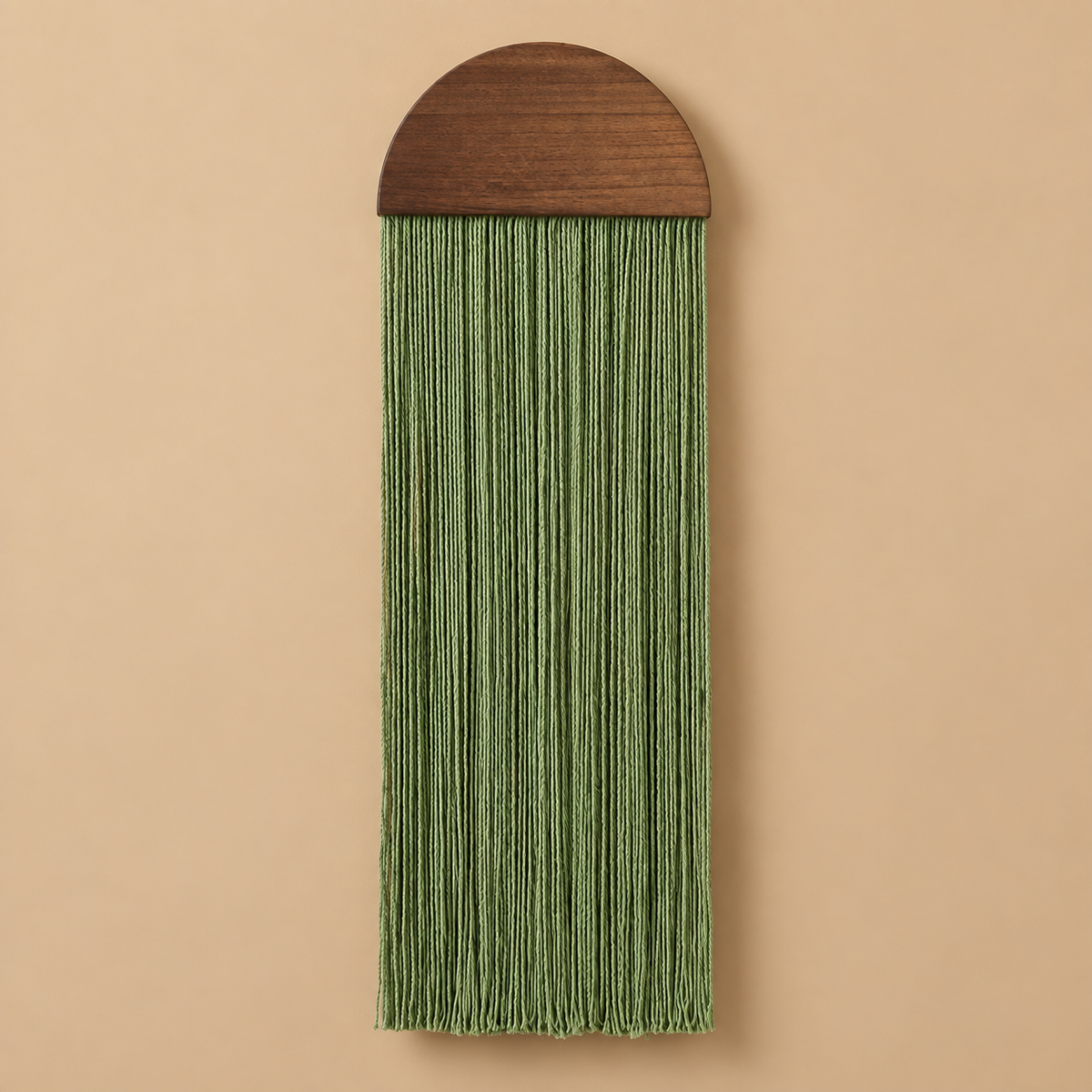 A vertical wall hanging with a dark brown wooden semicircular top and long fringe tassels in a muted sage green, shown