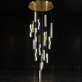 A modern multi-light chandelier with a circular brushed gold ceiling canopy and multiple cascading clear cylindrical crystal prisms, shown against a dark black background.