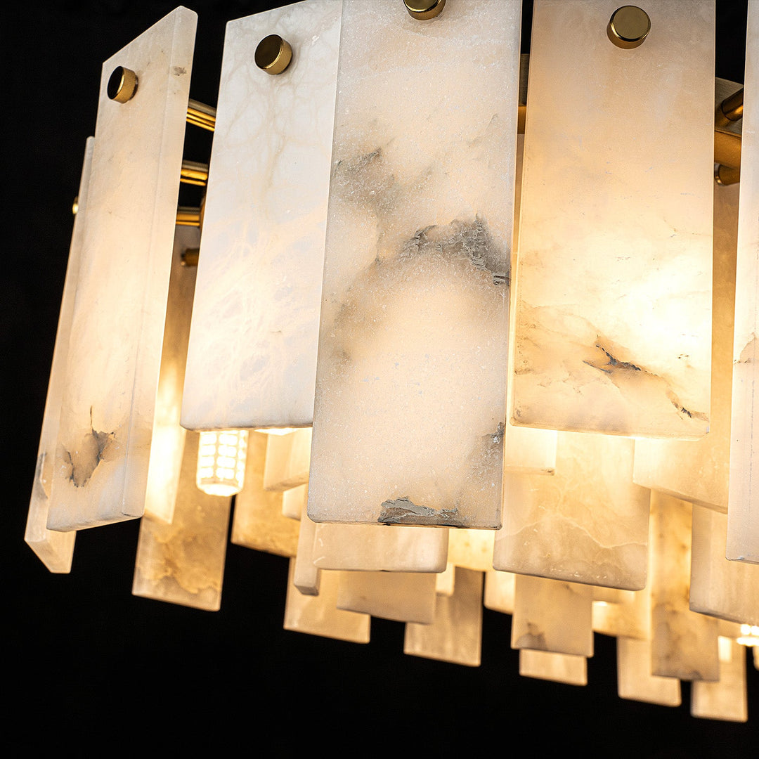 Pendant light close-up showing gray veining in white alabaster panels, round gold fasteners, and warm light against a black background.