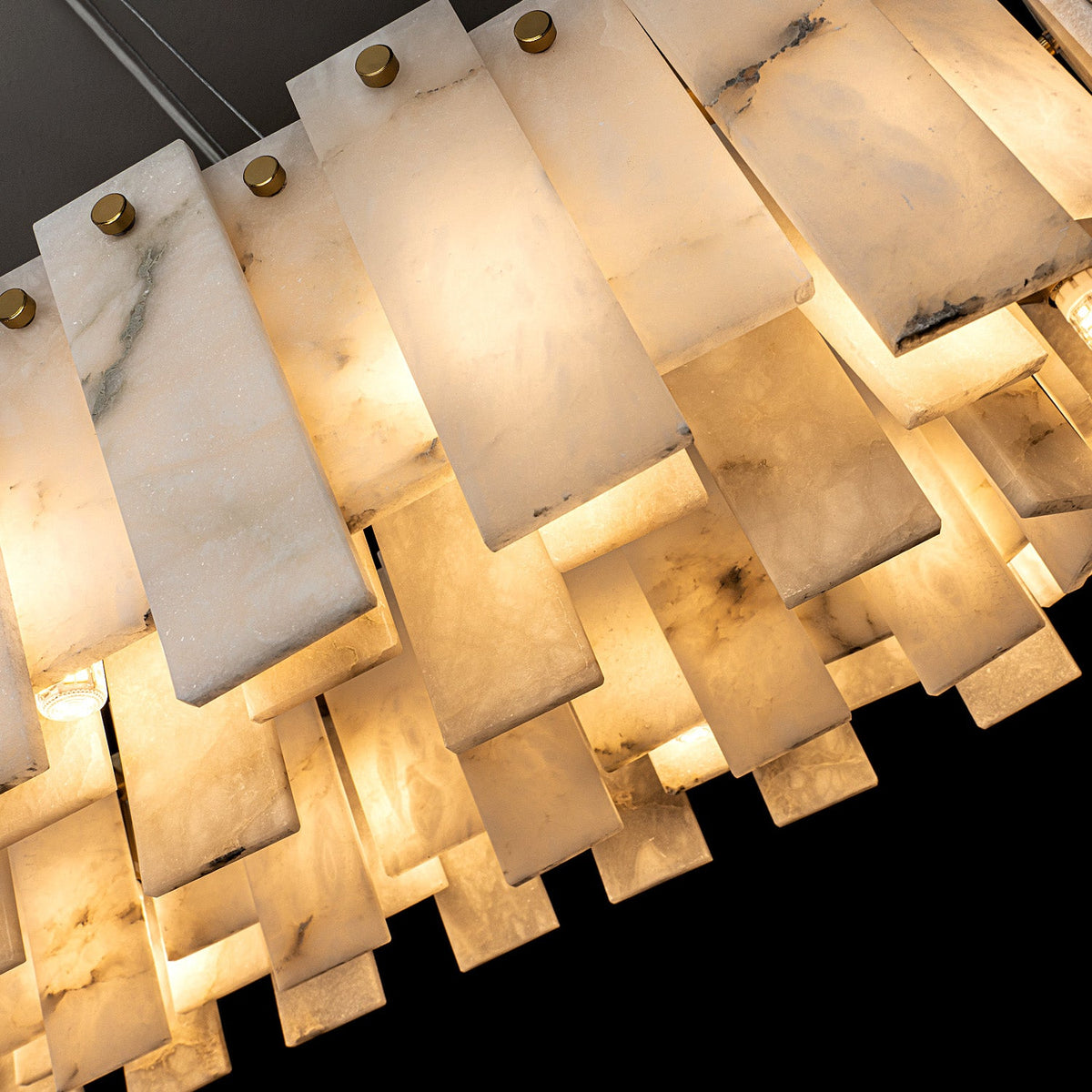 Angled close-up of the pendant light showing overlapping alabaster panels, gray veining, gold fasteners, and warm illumination.