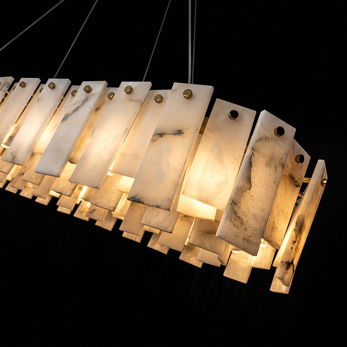 Linear pendant light with glowing cream alabaster panels, gray veining and gold-colored fasteners against a black background.