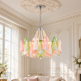 A pastel glass chandelier with pink, green, and white teardrop-shaped glass shades hangs from a silver chain in an ornate cream-colored room with classical wall moldings and a sofa below.