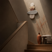 A minimalist interior staircase with warm wood steps and a textured plaster wall, decorated with a small stone sculpture, a terracotta vase with dried branches, and a small stool with a draped throw.