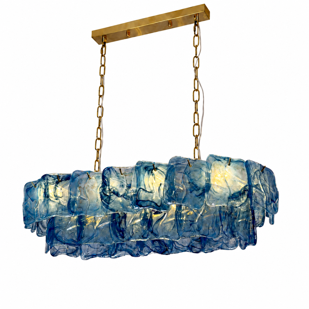 A linear chandelier with overlapping blue textured glass panels hangs from gold chains against a white background.
