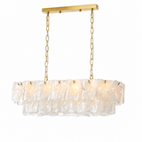 A linear chandelier with two tiers of clear textured glass hangs from gold chains against a white background.