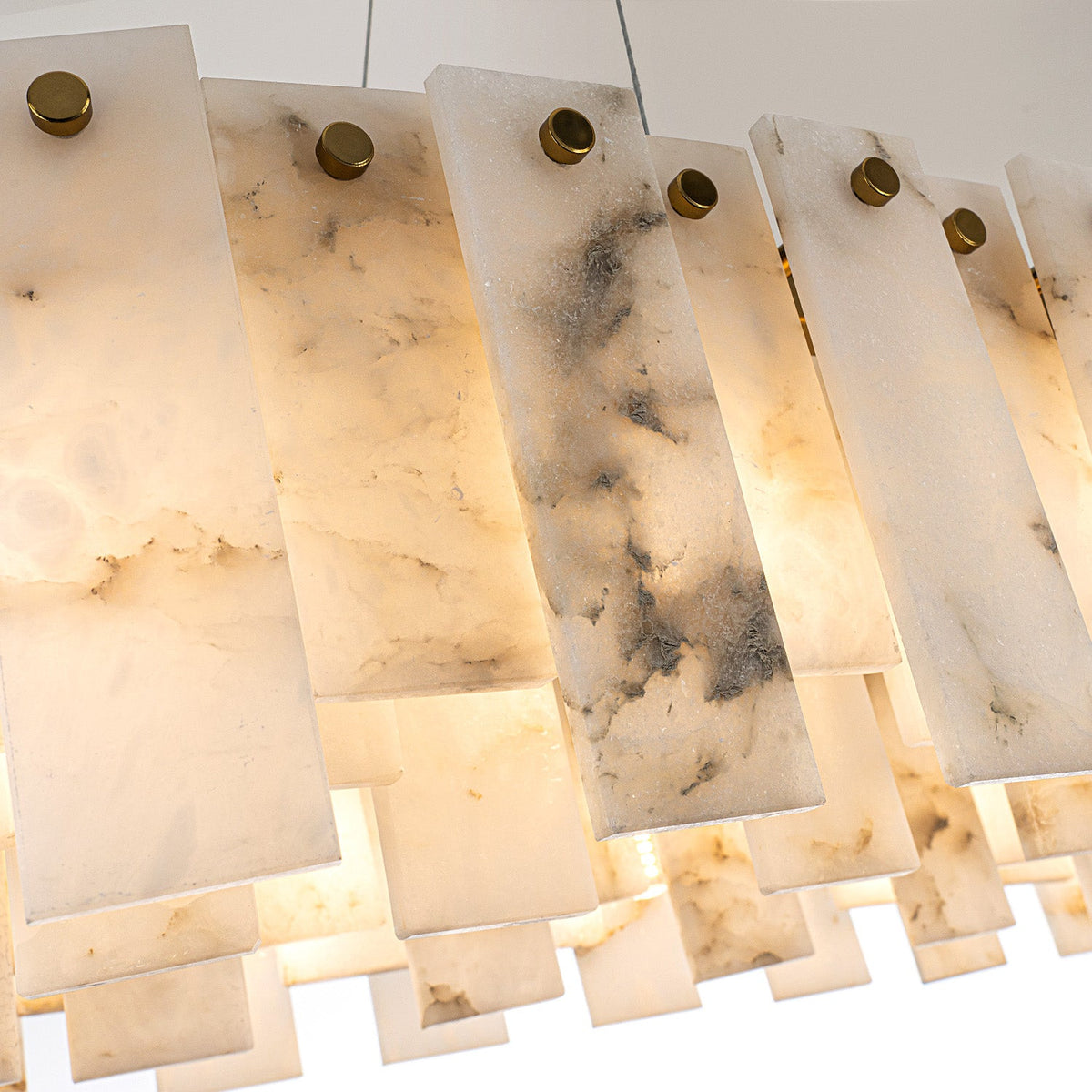 Pendant light close-up showing illuminated alabaster panels with gray veining, overlapping edges and round gold-colored fasteners.