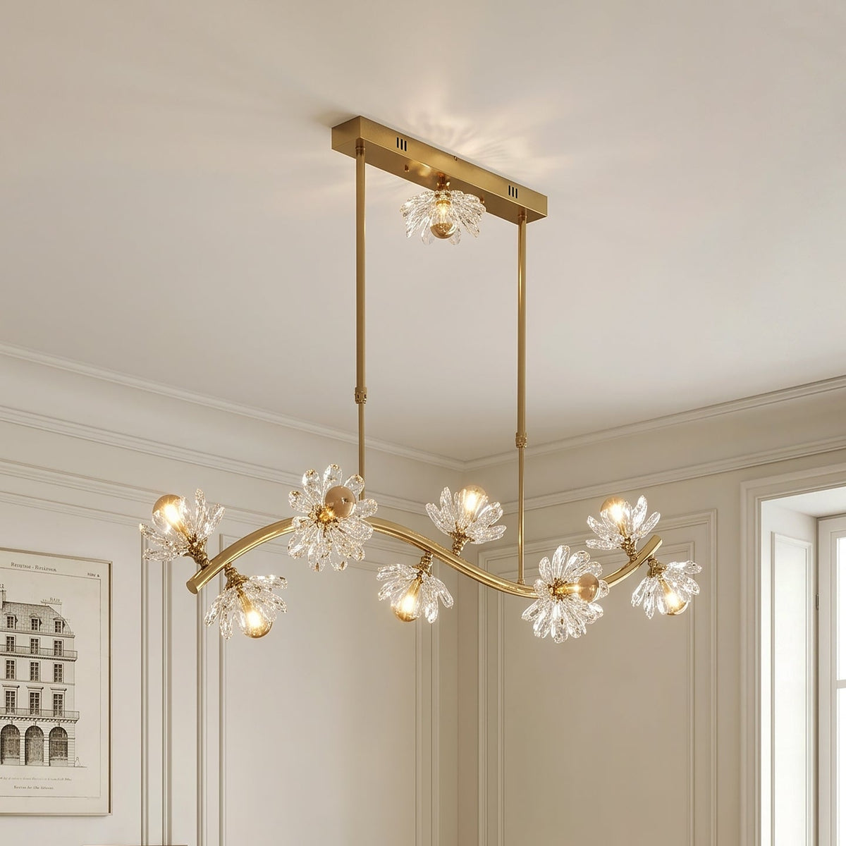 Gold chandelier with crystal accents hanging in a room with white walls and a framed picture.