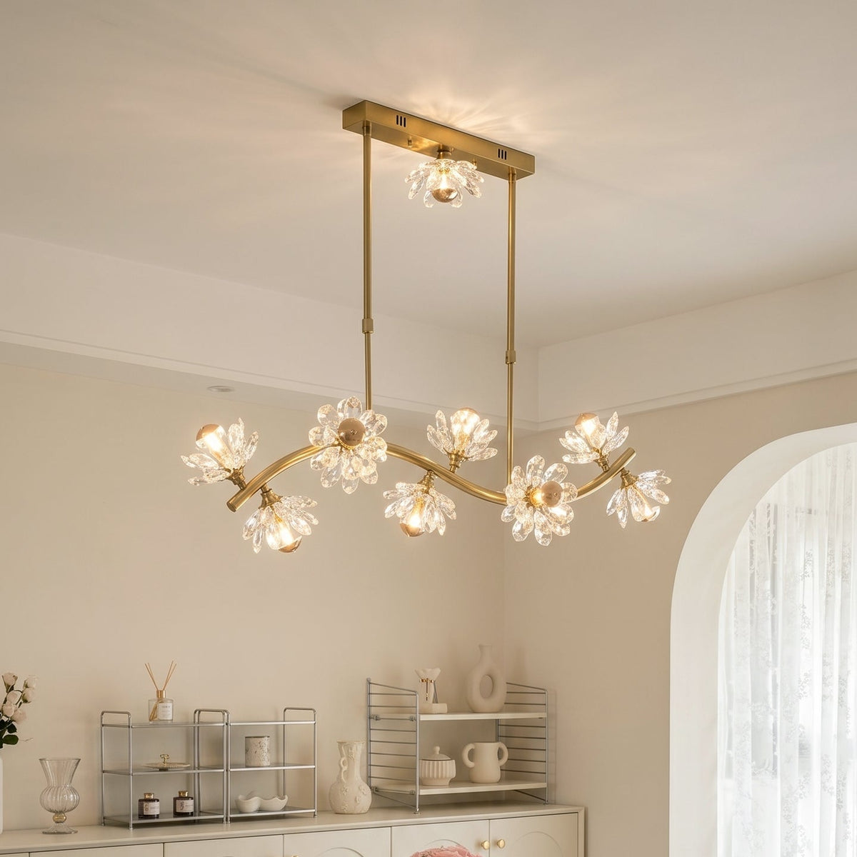 A modern multi-light chandelier with a gold-finished frame and clear crystal flower-shaped bulbs, hanging from the ceiling in a bright, neutral-toned dining or living room.