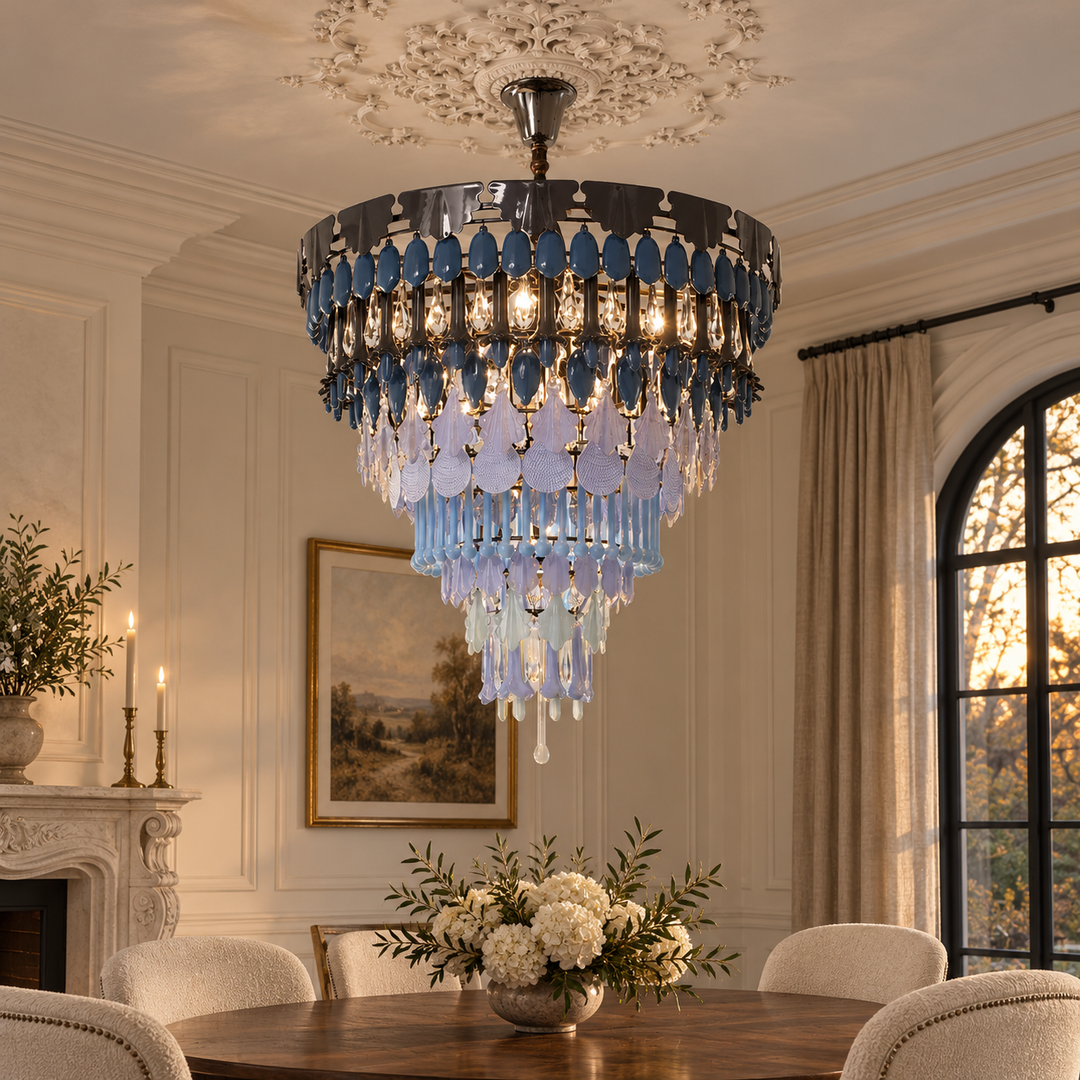 A large multi-tiered chandelier with blue and clear glass teardrop crystals hanging over a dining table in an elegant, classic room with a fireplace and arched window.