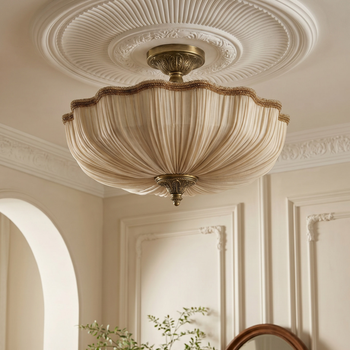 A vintage-style semi-flush mount ceiling light fixture with a pleated cream shade and antique brass hardware, shown installed on a decorative white plaster ceiling in an elegant room.