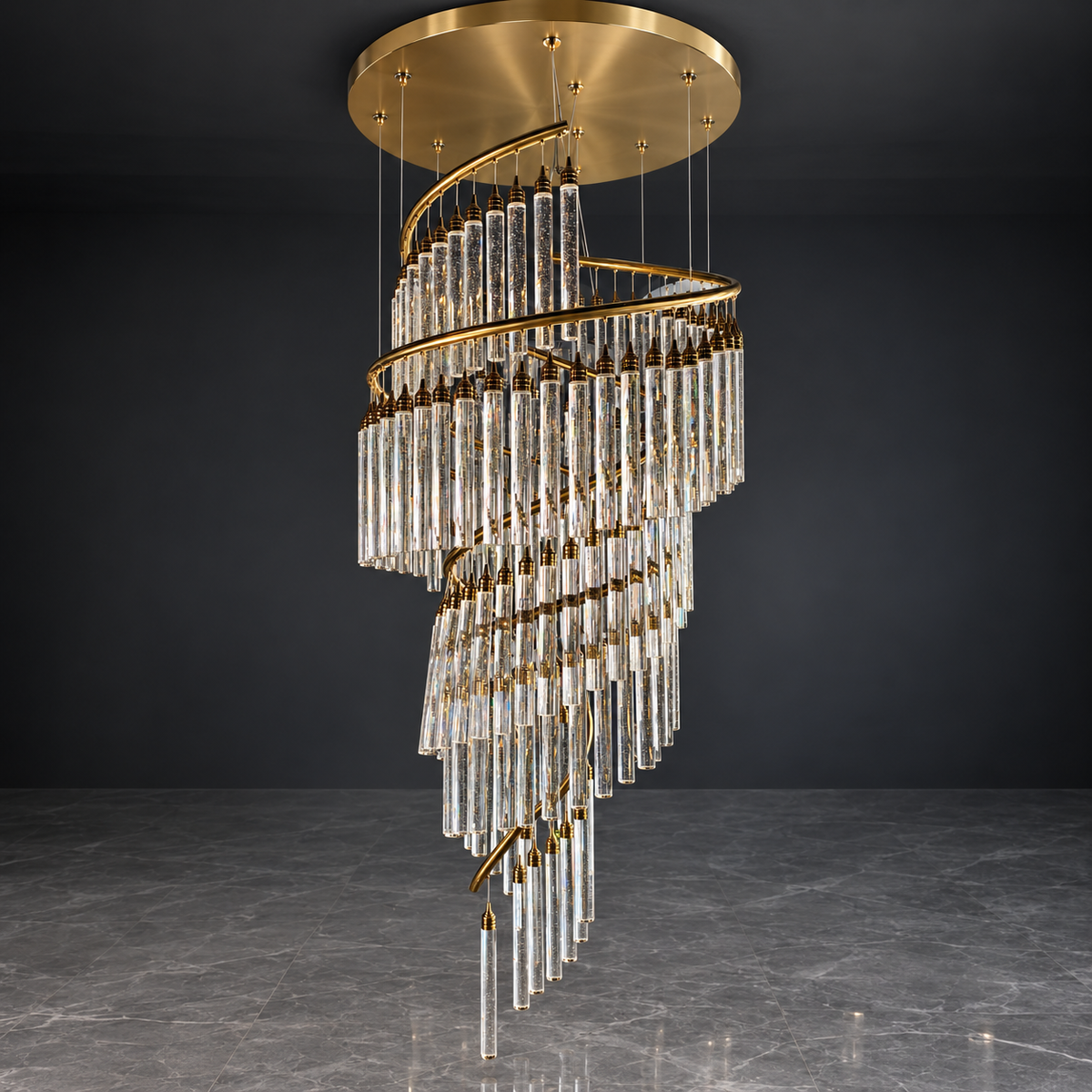 A modern spiral chandelier with clear glass cylindrical tubes and gold metal accents, suspended from a circular gold ceiling canopy against a dark gray wall and floor.