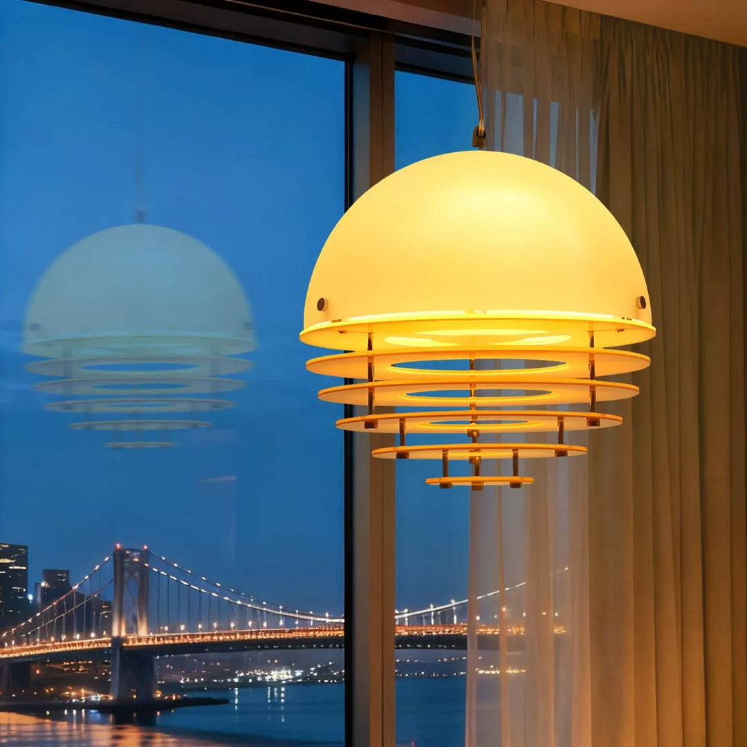 A modern dome-shaped pendant light with a glowing warm yellow-white shade and layered horizontal wooden rings, hanging in a room with a large window showing a city bridge at night.