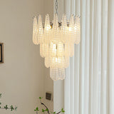 A modern tiered chandelier with textured, ribbed glass pendant lights in a warm white finish, hanging in a bright room with white vertical blinds and a beige wall.