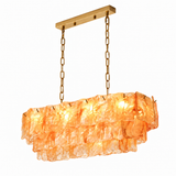Illuminated linear chandelier with tiered amber glass panels, gold-toned chains and a matching ceiling canopy against a white background.
