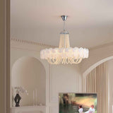 A multi-tiered chandelier with a white ruffled flower-like shade and hanging pearl beads, suspended from a silver ceiling canopy in a cream-colored room.