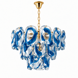 A modern chandelier featuring irregular, wavy clear glass shades filled with vibrant blue swirls, suspended from a polished gold chain and ceiling canopy against a solid white background.