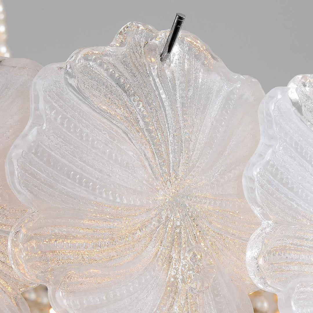 Close-up of a decorative chandelier light with translucent white glass petals and subtle gold glitter accents, showing a hanging metal rod against a soft gray background.