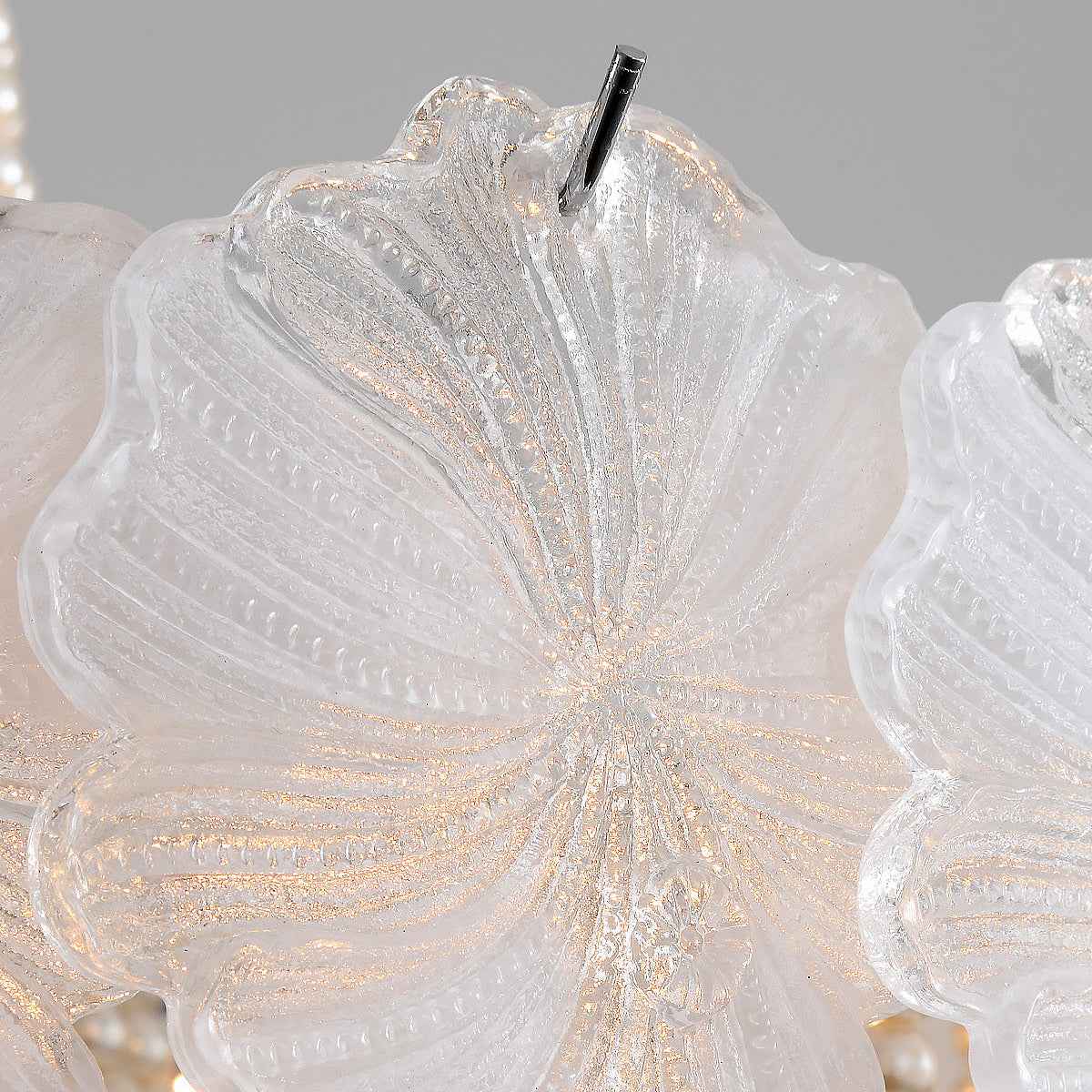 Close-up of a decorative chandelier light with translucent white glass petals and subtle gold glitter accents, showing a hanging metal rod against a soft gray background.