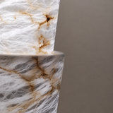 Close-up of the floor lamp’s stacked alabaster sections shows white and gray stone with brown veining against a gray background.