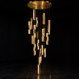 A modern multi-tier chandelier with a circular gold ceiling canopy, featuring numerous vertical crystal-encrusted tubes in varying lengths that dangle in a cascading arrangement against a dark background.