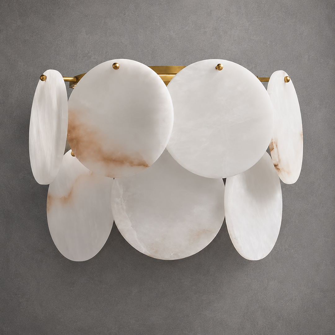 Wall sconce with white alabaster discs, subtle brown veining and brass fittings against a gray wall.