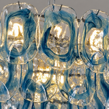 A close-up of a hanging glass chandelier or light fixture with multiple elongated oval glass shades. The shades are transparent and feature bold, swirling bands of deep cobalt blue and warm golden-yellow light filtering through.