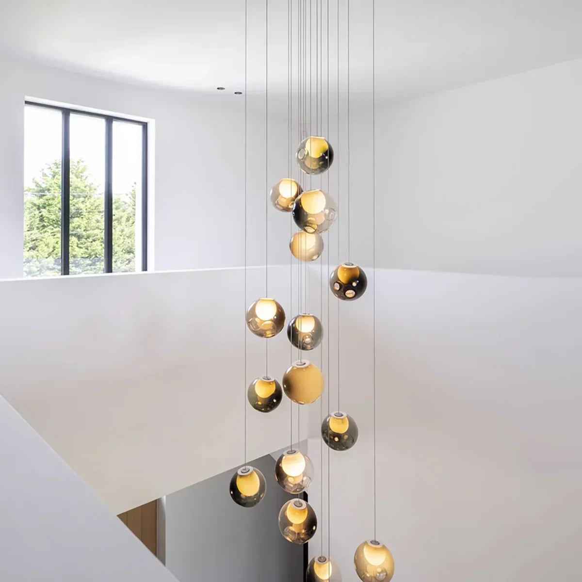 A modern multi-light chandelier with hanging spherical glass shades, shown suspended in a minimalist white interior space.
