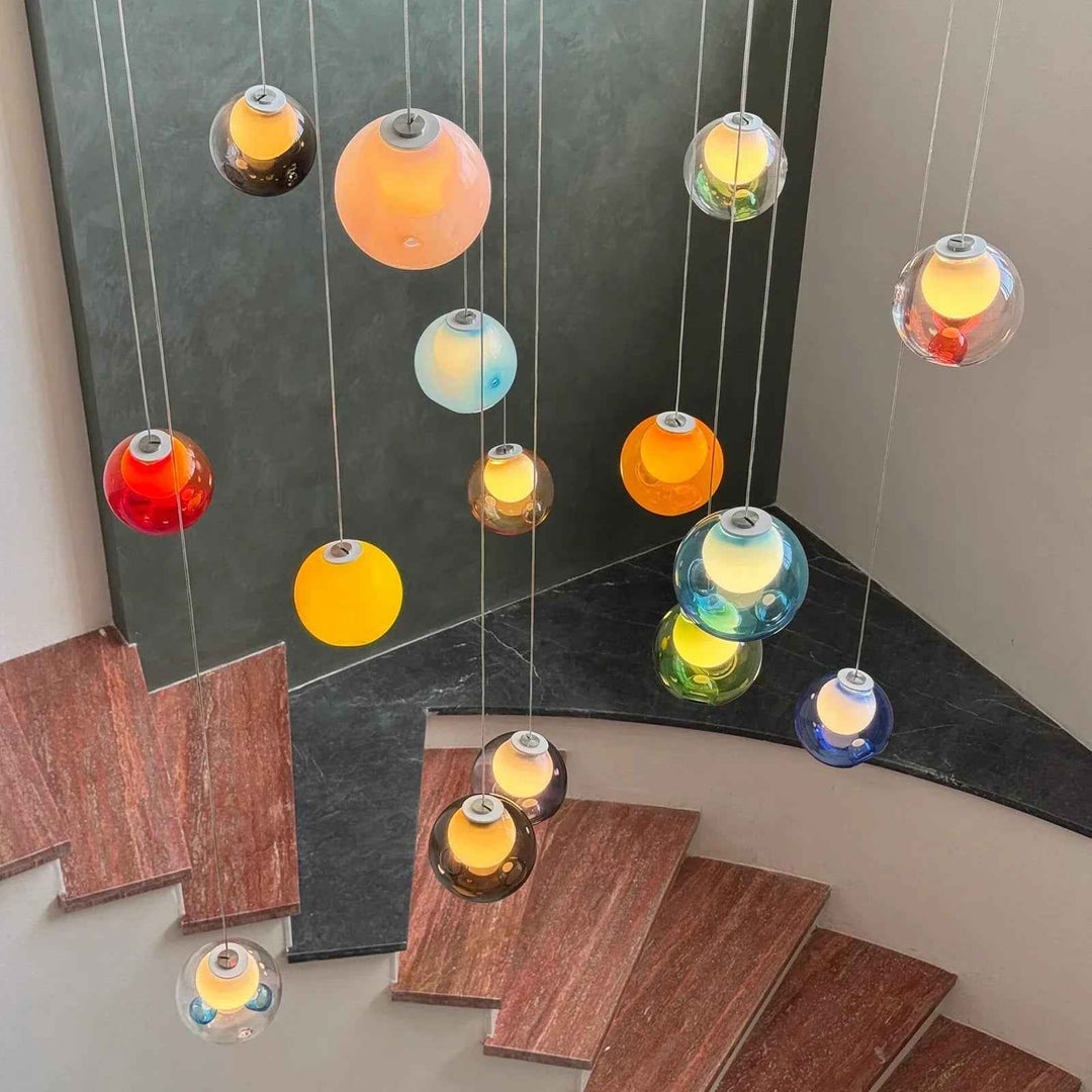 Multicolored glass globe chandelier cascading above a curved staircase with reddish steps and dark stone trim.