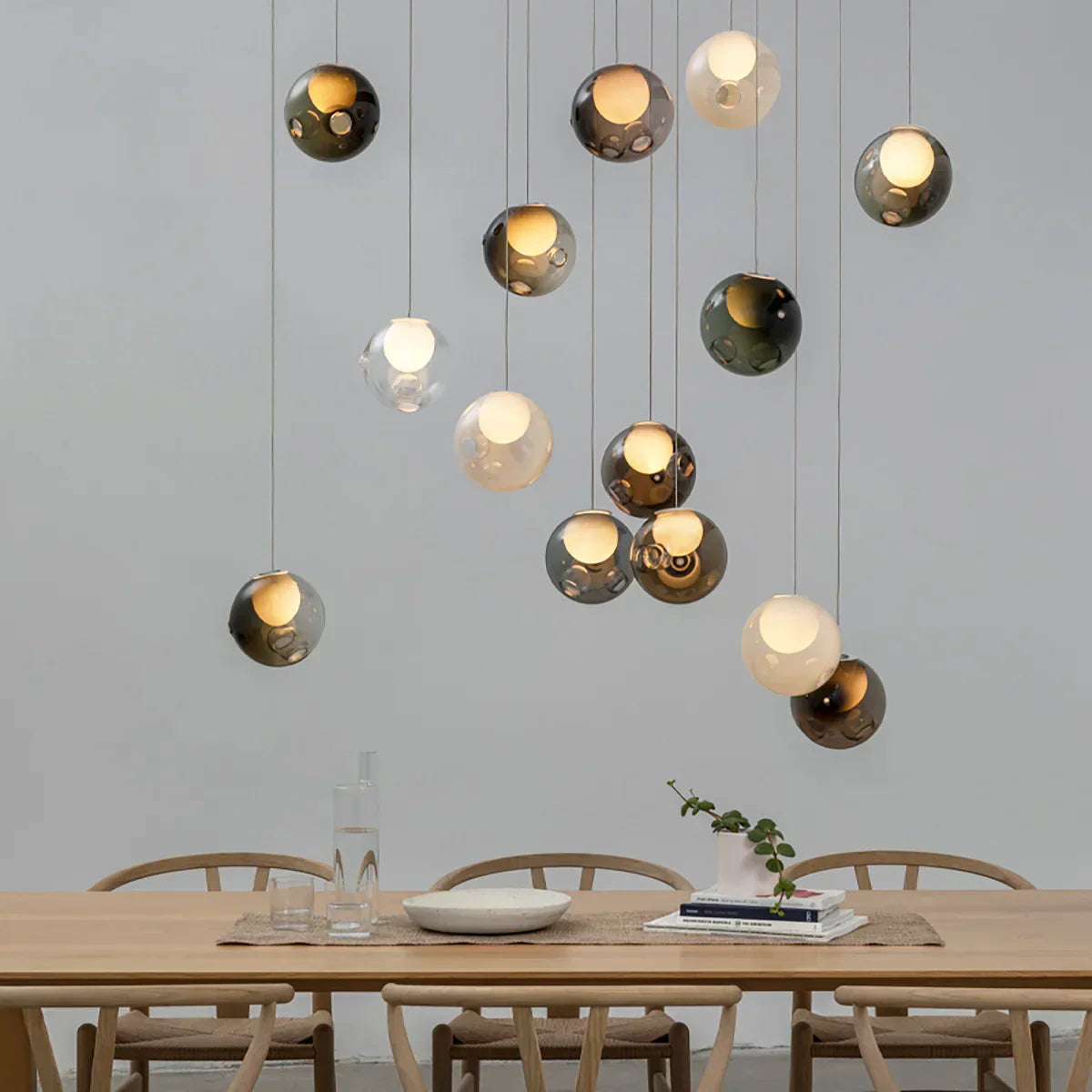 Chandelier with smoky and pale glass globes suspended above a wooden dining table surrounded by curved wooden chairs.
