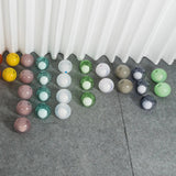 Glass globes for the chandelier in pink, teal, white, green, beige, and smoky purple sit on gray flooring beneath white curtains.