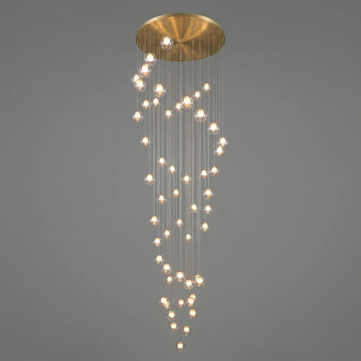 A modern multi-light chandelier with a brushed gold circular ceiling canopy and numerous clear glass spherical bulbs hanging in cascading vertical strands against a solid gray background.