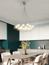 Modern chandelier hanging above a dining table in a kitchen with white chairs and a green wall.