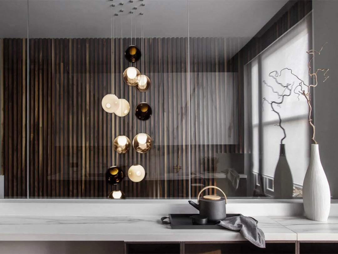 A cascading chandelier with smoky, clear and milky glass globes hangs behind a counter holding a teapot and tall vases.