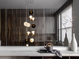 A cascading chandelier with smoky, clear and milky glass globes hangs behind a counter holding a teapot and tall vases.