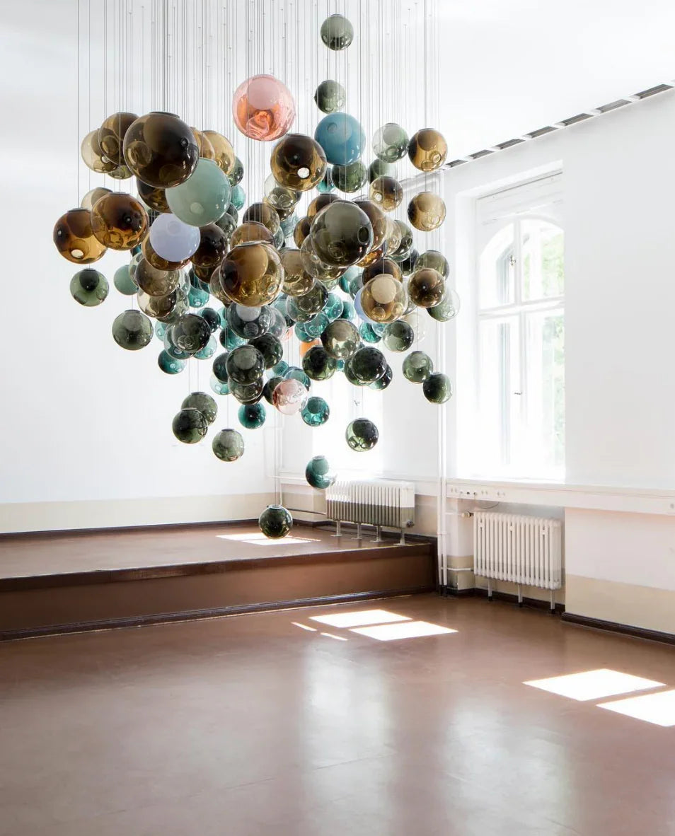 Colorful spherical chandelier hanging in a room with large windows and wooden floors.