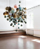 Colorful spherical chandelier hanging in a room with large windows and wooden floors.