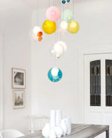 Chandelier cluster of pastel glass globes in pink, yellow, mint, and teal above a dining table in a white room