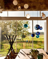 A chandelier with blue, teal, clear and milky glass globes hangs above a dining table beside large garden-facing windows.