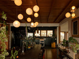 A chandelier with glowing milky and clear glass globes hangs beneath a wooden ceiling above a dining table adjoining a kitchen.
