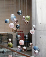 Colourful glass globe chandelier suspended on thin cables against a concrete wall beside a staircase
