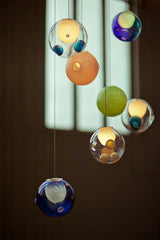 Multicolored glass globe chandelier with blue, green, amber, and clear shades hangs before a window in a dark interior.