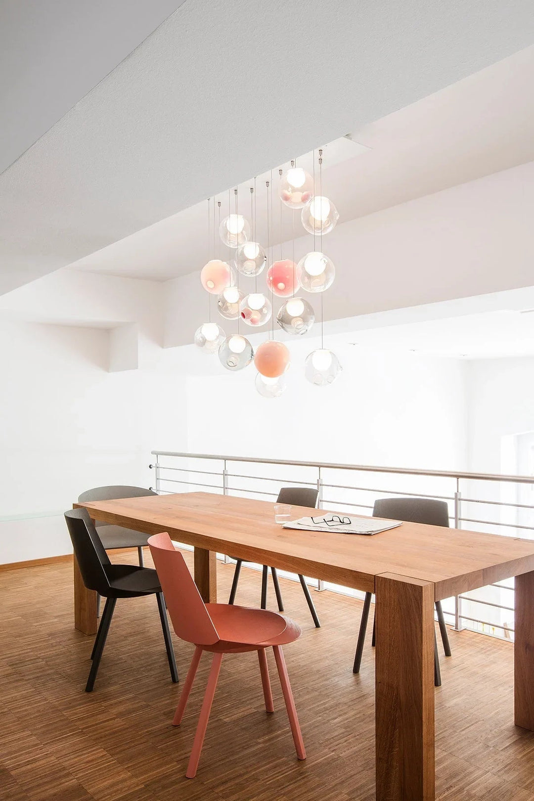 Glass globe chandelier with clear and pink shades hangs above a wooden dining table in a bright white room.